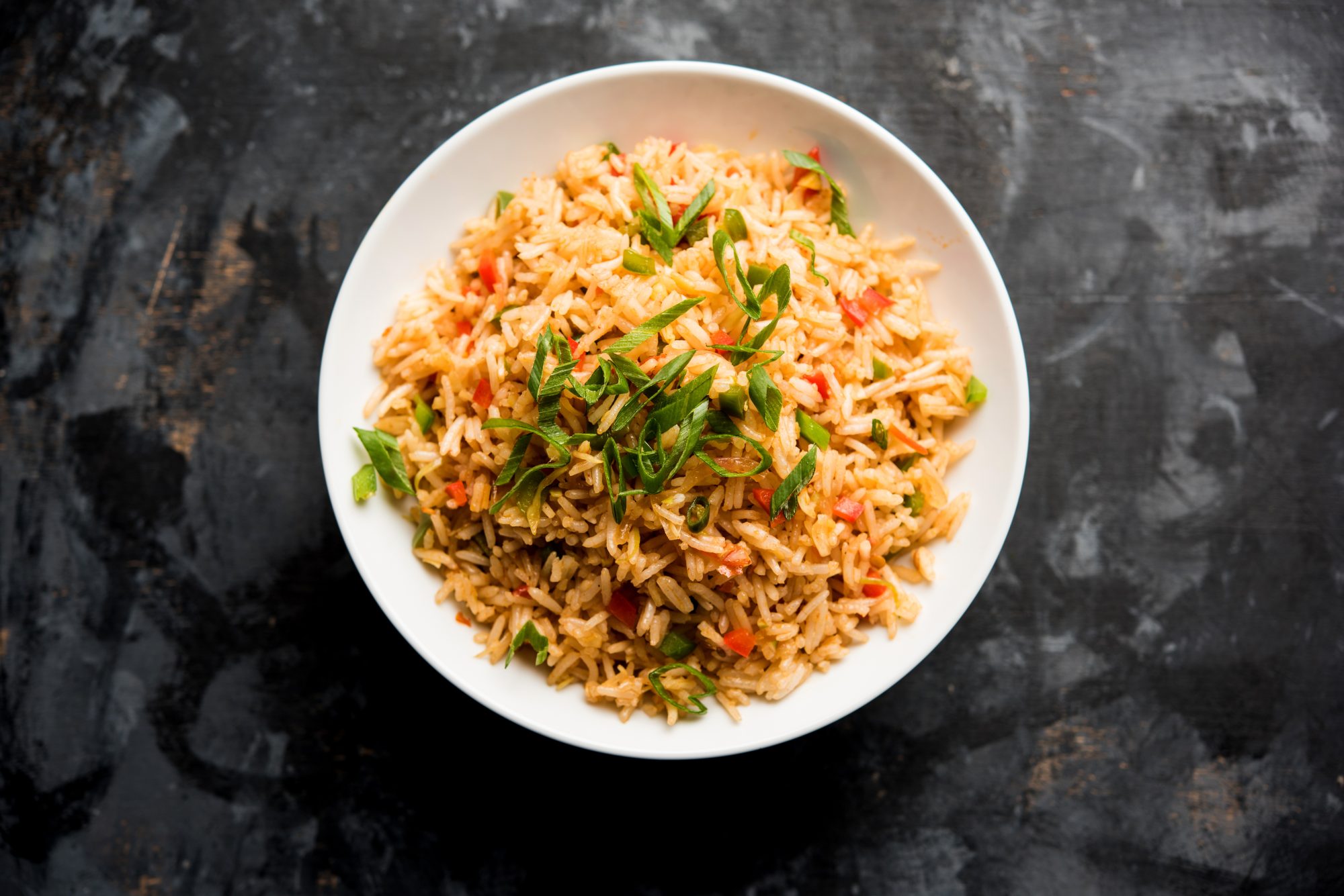 A bowl of fried rice on a black background, top view