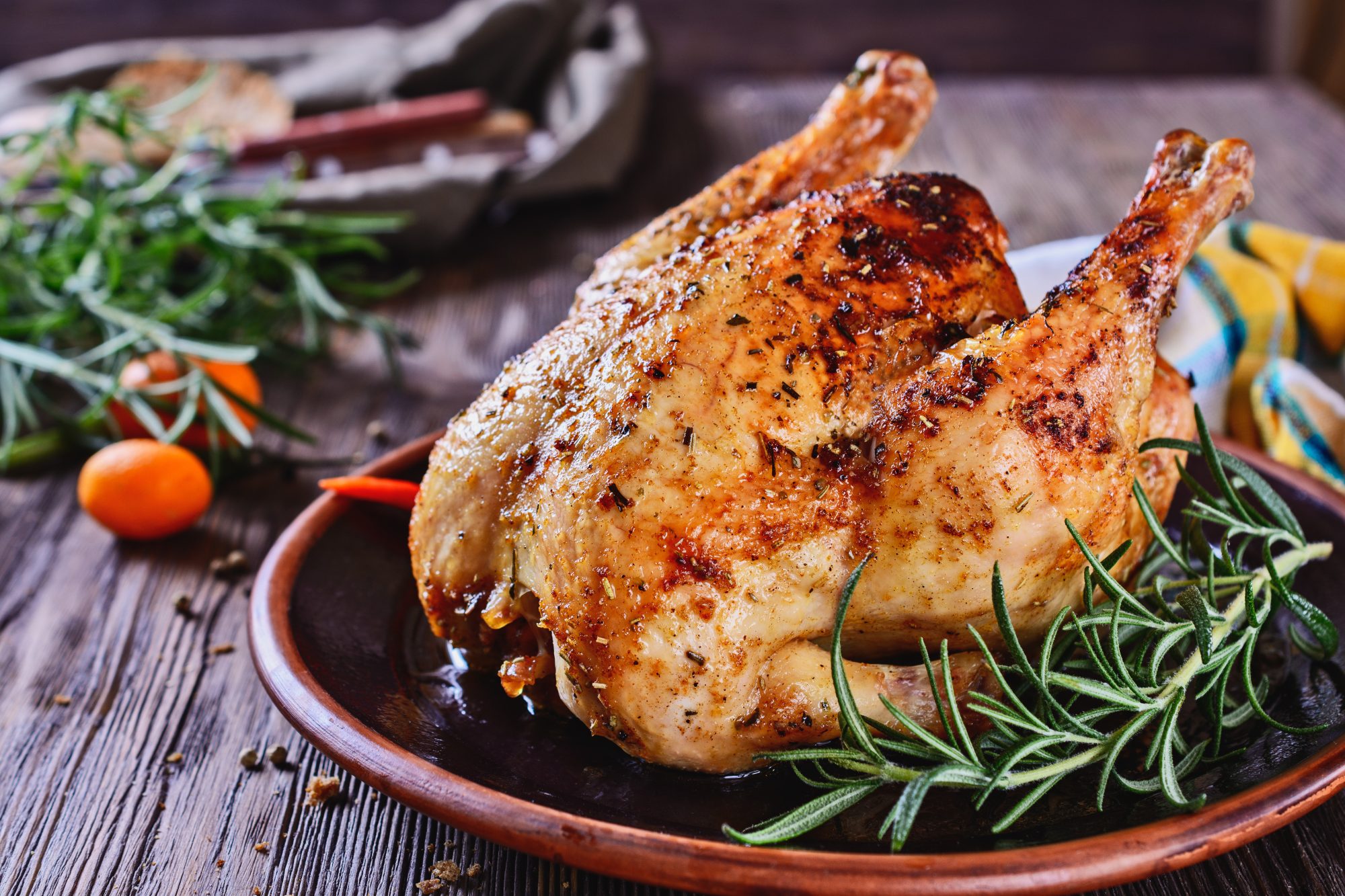 Freshly baked chicken is appetizing served on a ceramic dish next to a sprig of fragrant rosemary