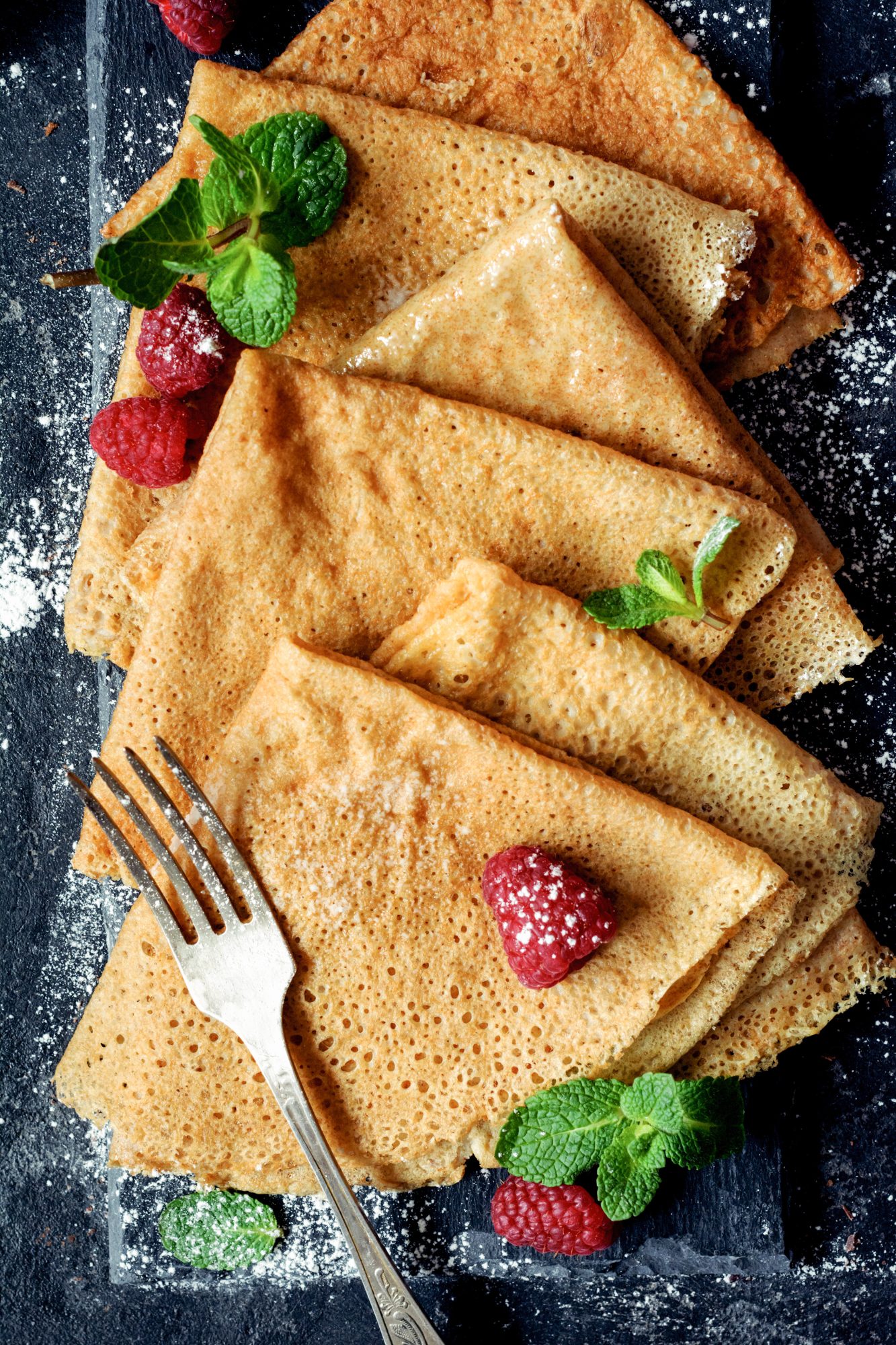 crepes with raspberries and mint on a dark background